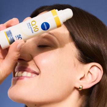 Kobieta uśmiecha się, zasłaniając oczy białym NIVEA Q10 Daily UV Fluid SPF 50. Widoczne logo i żółty akcent.