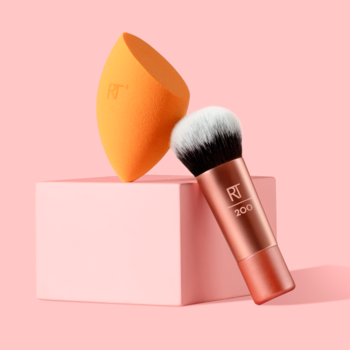 Pomarańczowa gąbka i pędzel Mini Expert Face Brush 200 z różowo-złotą rączką na różowym bloku.