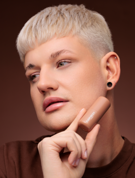 Zbliżenie na twarz mężczyzny z blond włosami trzymającego kremowy bronzer Everybody London Light w sztyfcie.