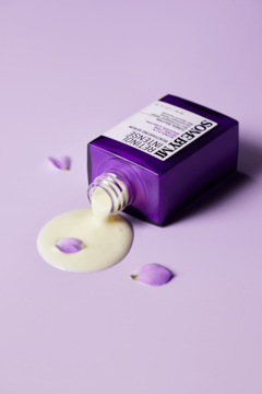 Fioletowa butelka serum Some By Mi Retinol Intense przewrócona, kremowy retinol wylewa się na liliowe tło.