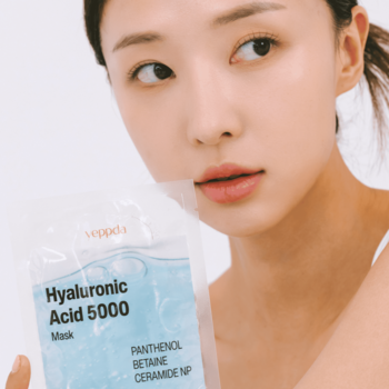 Zbliżenie na twarz kobiety, która trzyma nawilżającą maskę Yeppda Hyaluronic Acid 5000 z pantenolem w dłoni.