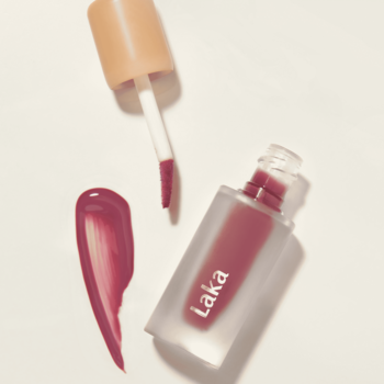 Laka Fruity Glam Tint Dewy, błyszcząca pomadka w płynie. Butelka, aplikator i błyszcząca próbka koloru na jasnym tle.