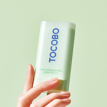 Zbliżenie jasnozielonego sztyftu Tocobo Cica Cooling Sun Stick SPF50+ z niebieskim napisem, trzymany w dłoni.