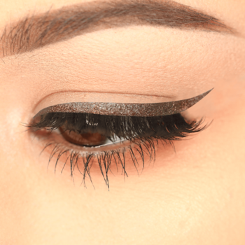 Zbliżenie oka z brązowym brokatowym eyelinerem J.Cat Beauty Dazzling Brown, tworzącym wyrazistą jaskółkę.