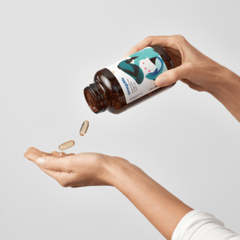OmegaMe Omega 3, ciemna butelka sypiąca złote kapsułki rybiego oleju do otwartej dłoni na jasnym tle.