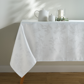 Biały obrus z subtelnym, żakardowym wzorem roślinnym, leżący na stole z białym serwisem do herbaty.