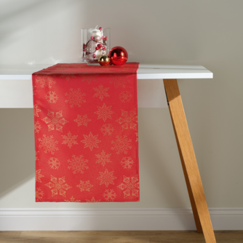 Czerwony bieżnik świąteczny ze złotymi śnieżynkami, rozłożony na białym stole z ozdobami.