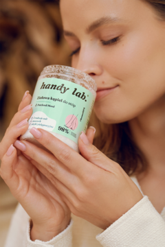 Ziołowa sól do stóp handy lab. Patchouli Mood w białym słoiku, którą kobieta wącha z przyjemnością.