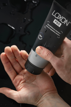 Ciemna tubka LOXON PRO szamponu na wypadanie włosów wyciskana na dłoń, krople wody na ciemnym tle.