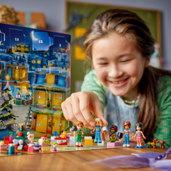 Uśmiechnięta dziewczynka układa figurki LEGO Friends z kalendarza adwentowego 2025 na świątecznej planszy.