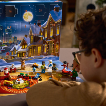 Dziecko patrzy na otwarty Kalendarz adwentowy LEGO City 2025. Na macie świąteczne minifigurki i mini-modele.
