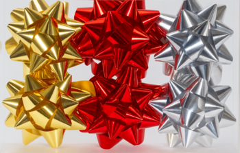 Zbliżenie na trzy błyszczące kokardki prezentowe: złotą, czerwoną i srebrną, na jasnym tle.