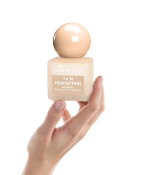 Kobieta trzyma w dłoni beżowy podkład Bielenda Skin Perfection kryjąco-wygładzający, widok z przodu.