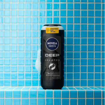 Czarny szampon NIVEA MEN Deep z czarnym węglem, z białymi mydlinami na tle niebieskich kafelków.