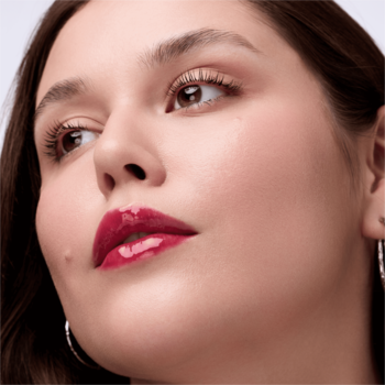 Zbliżenie na lśniące, śliwkowe usta kobiety z odżywczym olejkiem Catrice Glossin' Glow 070 Make A Move.