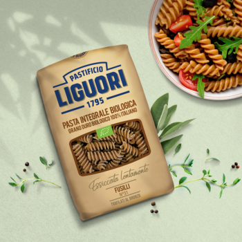 Brązowe opakowanie makaronu Liguori Fusilli Integrale BIO na stole z daniem i świeżymi ziołami.