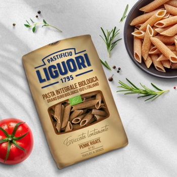 Makaron pełnoziarnisty Liguori Penne Rigate BIO w brązowym worku, widok z przodu, z pomidorem i ziołami.
