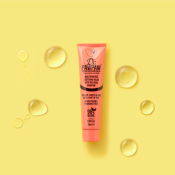 Wielozadaniowy koralowy balsam Dr. PawPaw Tinted True Coral na żółtym tle, otoczony błyszczącymi kroplami oleju.