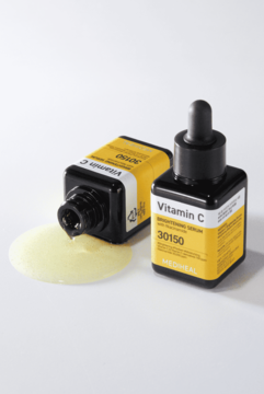 Mediheal Vitamin C Brightening Serum 30150 w dwóch ciemnych butelkach; jedna leży, rozlewając żółty płyn.