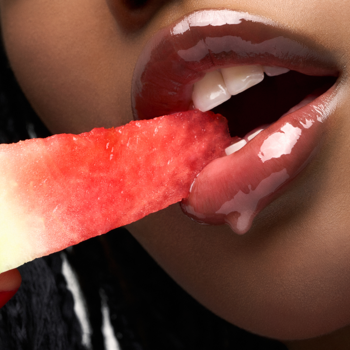 Zbliżenie na lśniące usta, które jedzą kawałek arbuza. Efekt luksusowego olejku do ust Fresh Watermelon.