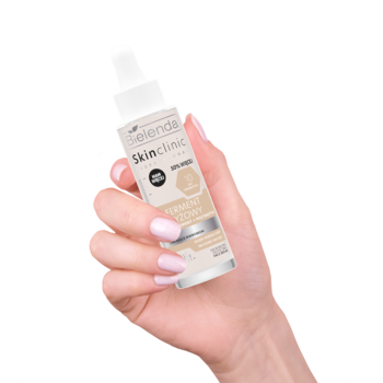 Bielenda Skin Clinic Ferment Ryżowy serum do twarzy, biała butelka z pompką, trzymana w dłoni z różowym manicure.