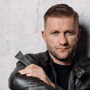 Mężczyzna w skórzanej kurtce trzyma nawilżający krem do twarzy dla mężczyzn w czarnej tubce, koi podrażnienia.