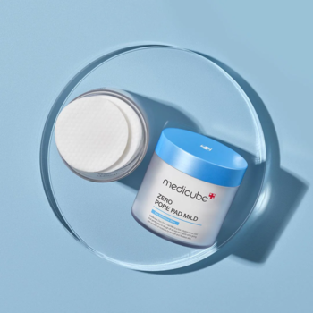 Medicube Zero Pore Pad MILD, złuszczające płatki. Otwarty słoik z niebieską nakrętką, białe pady, jasnoniebieskie tło.