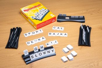 Gra Rummikub Eco Słowny z tekturowymi kostkami na drewnianym stole, widok z góry z ułożonymi słowami.