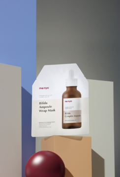 Ma:nyo Bifida Ampoule Wrap Mask i serum Bifida Complex w butelce z dropperem, na kolorowych blokach.