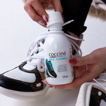 Coccine Sole Cleaner 125 ml w białej butelce, trzymany ręką obok białego sneakersa z brązowymi detalami.