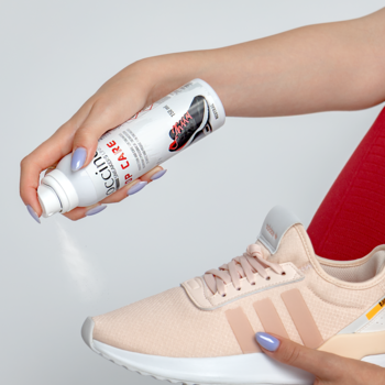 Dłoń spryskuje jasnoróżowy sneakers uniwersalnym sprayem Cocciné Top Care. Pielęgnuje i odświeża obuwie.