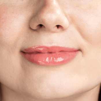 Lumene Lip Glow Oil Balm Juicy na ustach. Zbliżenie na błyszczące, nawilżone usta z koralowym, dziewczęcym połyskiem.
