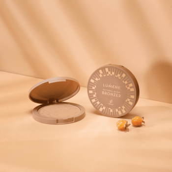 Dwa okrągłe bronzery Lumene Natural Glow Arctic Sun, otwarty i zamknięty, z malinami moroszkami na beżowym tle.