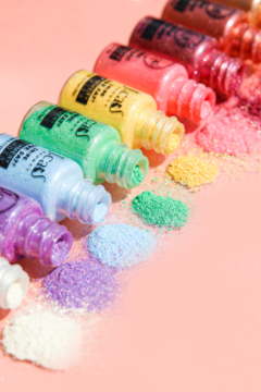 Kolorowe sypkie pigmenty glitter w małych buteleczkach ułożone ukośnie na różowym tle, efekt blasku.