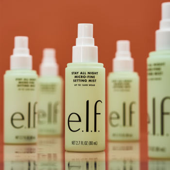 Jasnozielony e.l.f. Stay All Night Micro-Fine Setting Mist, spray utrwalający makijaż, na pomarańczowym tle.