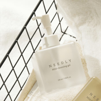 Biały Needly Mild Cleansing Gel w prostokątnej butelce z pompką, widok z przodu, na białym ręczniku i w koszu.