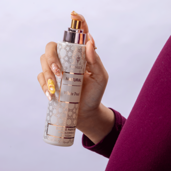 Biały spray do ciała "Natural Milk & Pearl" ze złotym ornamentem, w dłoni z ozdobnymi paznokciami.