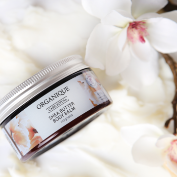 Balsam do ciała Organique Shea Butter Body Balm Magnolia w słoiczku na białym, puszystym tle z orchideami.