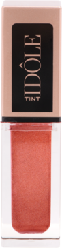 Lancôme Idôle Tint Sand Storm, koralowy płynny cień i róż w butelce, czarno-złota nakrętka 'IDÔLE TINT'.