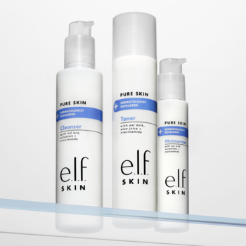 Trzy białe butelki elf SKIN Pure Skin: Cleanser z pompką, Toner w sprayu i Moisturizer, na niebieskiej półce.