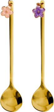 Dwie długie złote łyżeczki z ozdobnymi uchwytami w kształcie kwiatów – różowego i fioletowego – stojące pionowo.