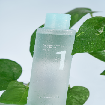Numbuzin No.1 Pure-Full Calming Herb Toner w przezroczystej butelce z niebieską nakrętką, na tle zielonych liści.