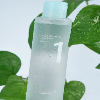 Numbuzin No.1 Pure-Full Calming Herb Toner, zbliżenie matowej butelki z kroplami wody, niebieską nakrętką, otoczonej liśćmi.