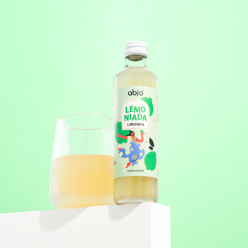Naturalna abio Lemoniada Limonka w szklanej butelce, obok napój w szklance, na zielonym tle.