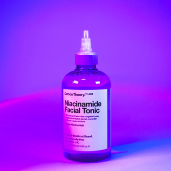 Carbon Theory Niacinamide Facial Tonic, przezroczysta butelka z fioletowym płynem i białą etykietą, neonowe światło, widok z przodu.
