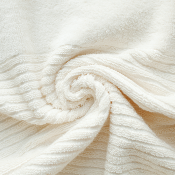 Miękki, ecru koc ryflowany, złożony w spiralę, ukazujący puszystą, welurową teksturę materiału z bliska.