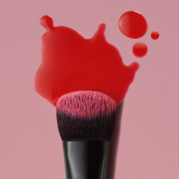 Skośny pędzelek e.l.f. do blendowania różu w płynie, z syntetycznym włosiem, na różowym tle, z czerwonym makijażem.