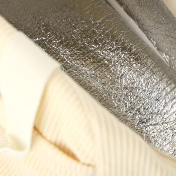 Zbliżenie na kremowy, prążkowany materiał obok pogniecionej, błyszczącej srebrnej tkaniny. Detal tekstur.