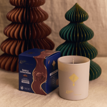 Biała świeca E. Wedel x Candly & Co o zapachu czekolady, z niebieskim pudełkiem i świątecznymi drzewkami.