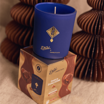 Niebieska świeca E. Wedel x Candly & Co o zapachu karmelowej czekolady na złotym pudełku, z tyłu brązowe ozdoby.